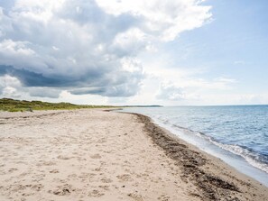 Una playa con arena, una zona de dunas cubiertas de hierba y un cielo nublado.