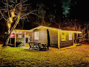 A small, single-story building with a porch and a picnic table, surrounded by trees. - 4 Person Holiday Home in Frederiksvaerk (Frederiksvaerk)