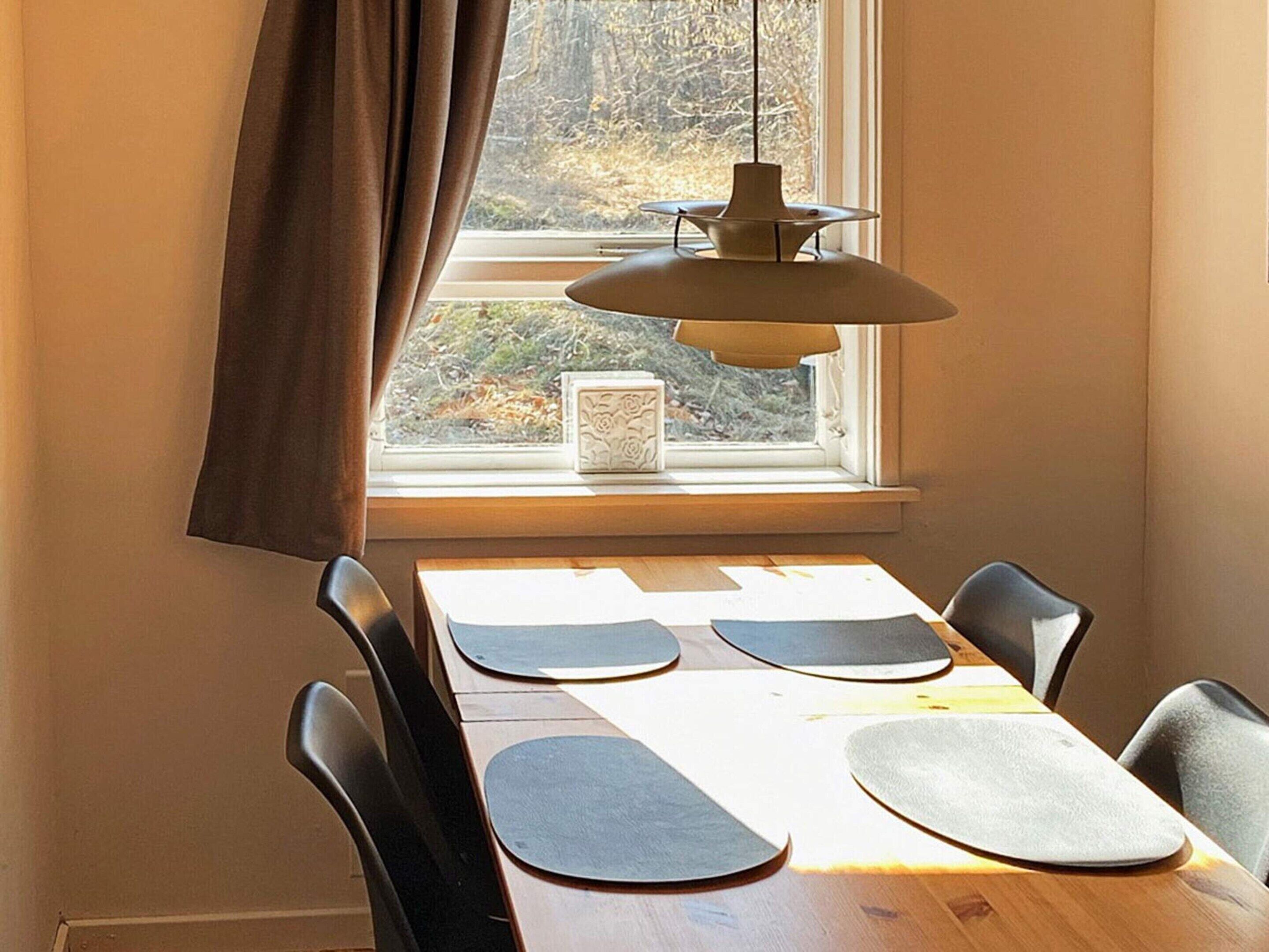A dining area with a table set for four, a window with curtains, and a pendant light.