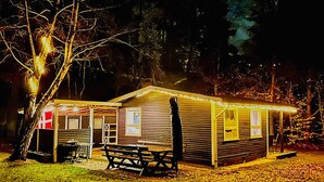 A small, single-story building with a porch and a picnic table, surrounded by trees. - 4 Person Holiday Home in Frederiksvaerk (Frederiksvaerk)