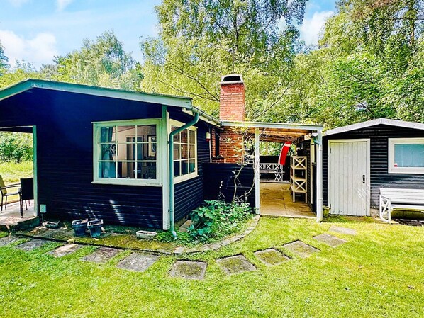 A small, single-story house with a dark blue exterior, a brick chimney, and a covered porch area. - 4 Person Holiday Home in Frederiksvaerk (Frederiksvaerk)