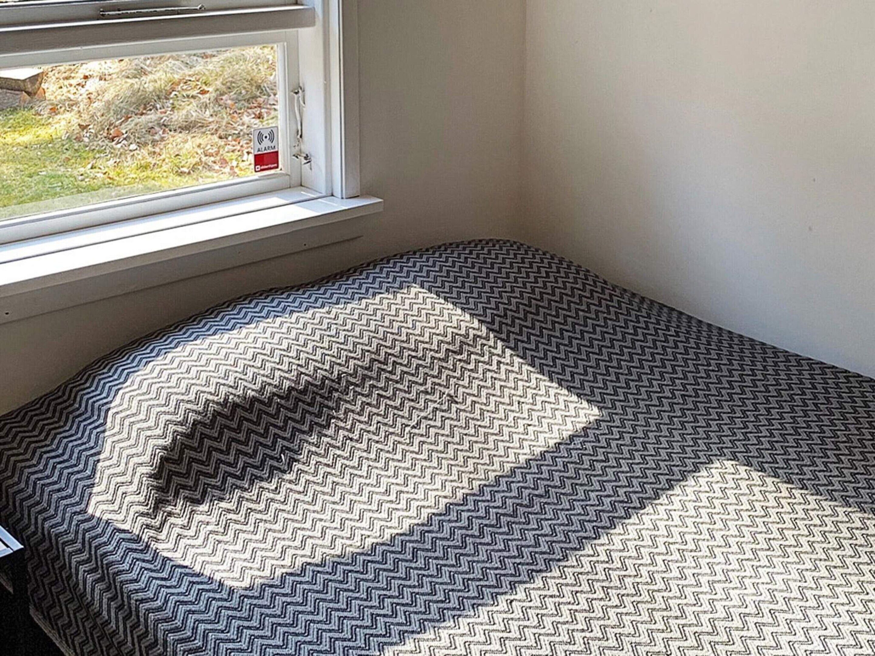 Una habitación con ventana, cama con colcha estampada y vista al exterior.