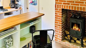 A kitchen with a brick fireplace, a coffee maker, and a shelf with various items.