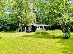 A house with a porch, surrounded by a well-maintained lawn and dense trees. - 4 Person Holiday Home in Frederiksvaerk (Frederiksvaerk)