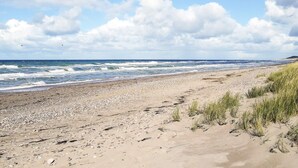 En strand med en klippefyldt kystlinje, bølger og et delvist overskyet himmelbillede.