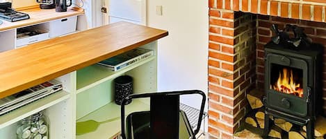 A kitchen with a brick fireplace, a coffee maker, and a shelf with various items.