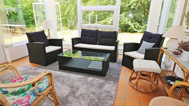 A sunlit room with wicker furniture, a glass coffee table, and a view of lush greenery outside. - 6 Person Holiday Home in Hadsund (Hadsund)