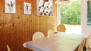 A dining area with a wooden wall, a table with a checkered tablecloth, and chairs. There are framed botanical prints on the wall and a dish rack with plates and bowls. - 6 Person Holiday Home in Hadsund (Hadsund)