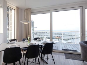 A dining area with a table set for four, large windows with a view of the sea and a pier, and a balcony with a view of the sea. - 5 Star Holiday Home in Wendtorf (Wendtorf)