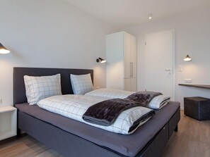 Un dormitorio moderno con una cama grande, dos mesitas de noche, un armario e iluminación en la pared.