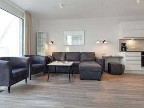 A modern living room with a sofa, a coffee table, and a kitchen area with a coffee machine.