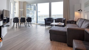 Ein modernes Wohnzimmer mit einer Couch, Sesseln, einem Esstisch und einem Fernseher.
