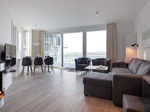 A modern living room with a sofa, armchairs, a dining table, and a TV. - 5 Star Holiday Home in Wendtorf (Wendtorf)