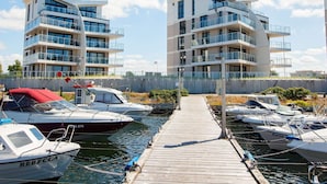 A marina with modern apartment buildings, boats docked, and a wooden walkway.