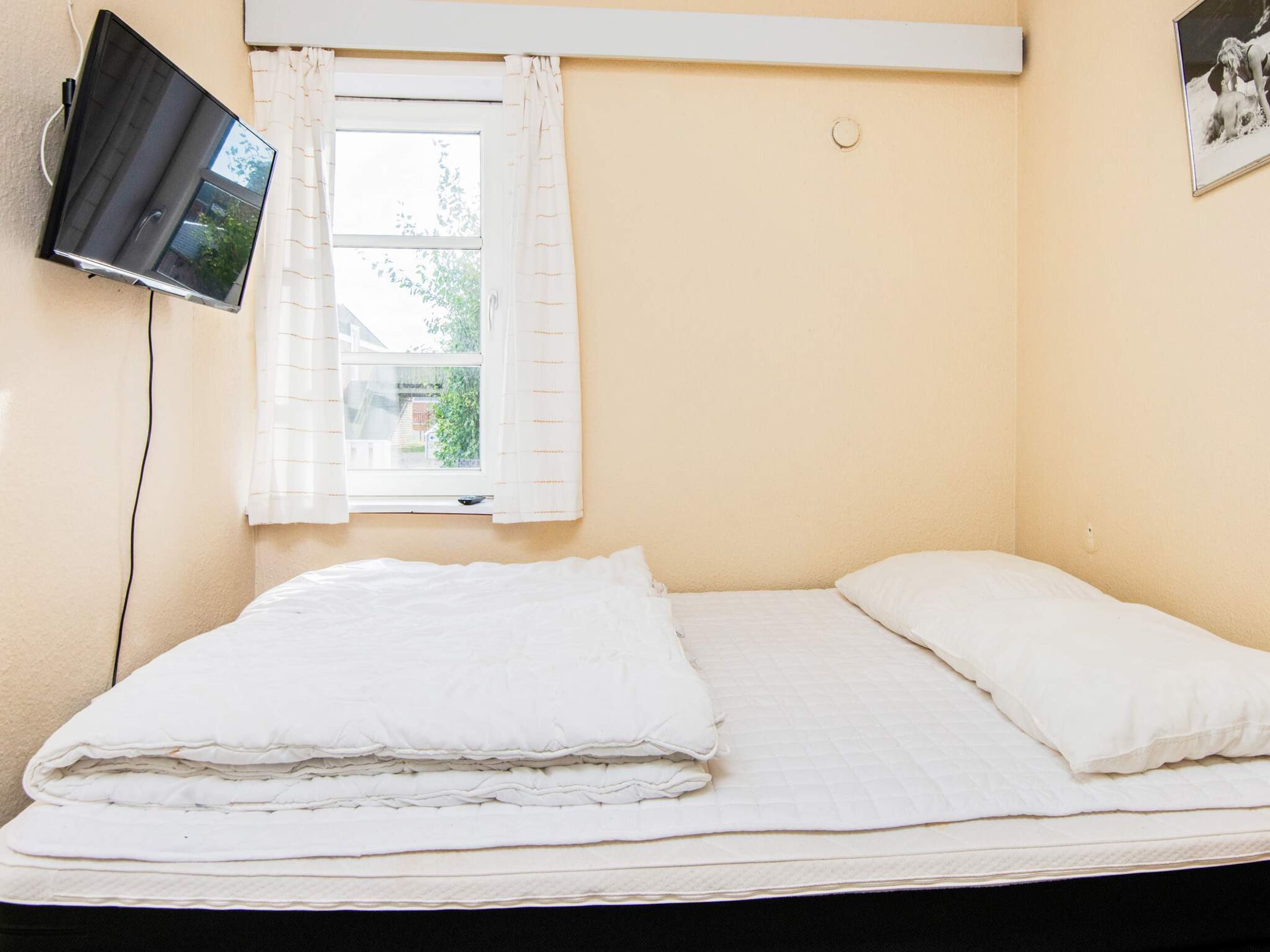 A single bed with white bedding, a window with white curtains, and a wall-mounted television.