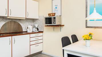 A compact kitchen with white cabinets, a microwave, a coffee maker, and a small dining table with chairs.