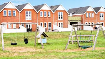 A playground with swings and a tire swing, set against a backdrop of red brick buildings with white trim.
