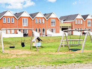A playground with swings and a tire swing, set against a backdrop of red brick buildings with white trim.