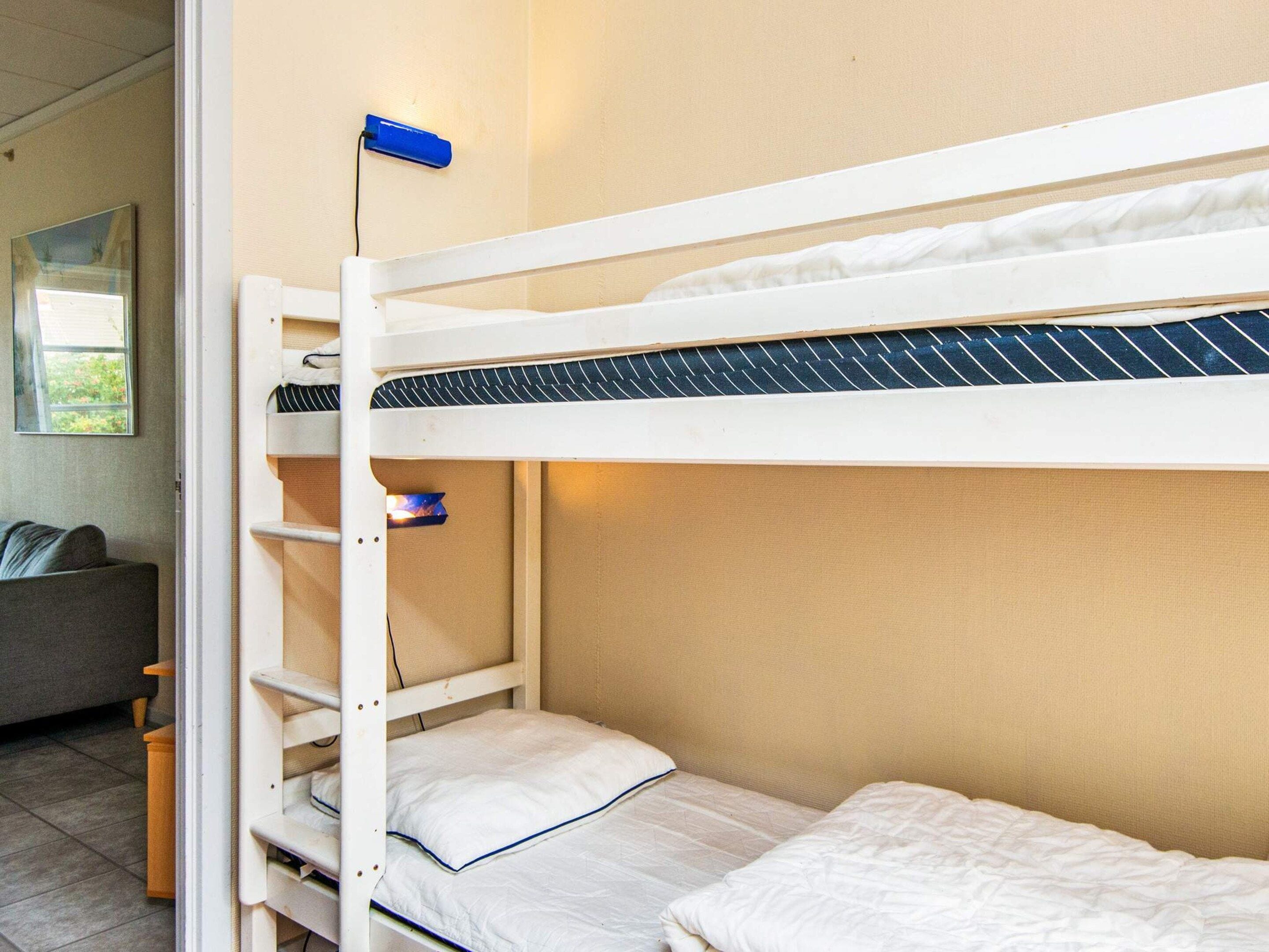 Ein Etagenbett mit einem blauen Gegenstand im oberen Bett, ein graues Sofa und ein Fenster mit Blick auf Grünflächen.