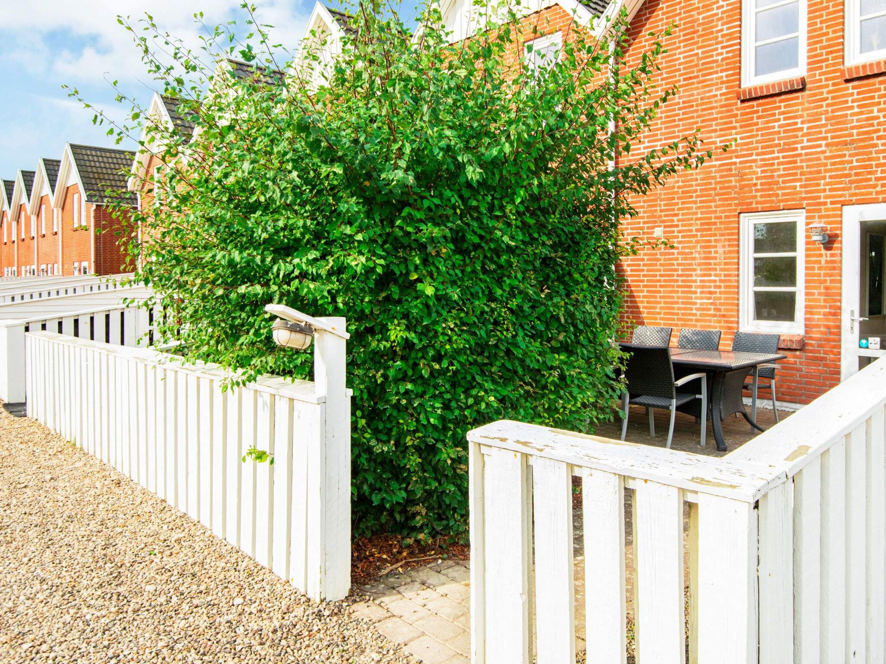 A residential property with a white picket fence, a brick house, and a patio area with outdoor furniture.