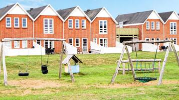 A playground with swings and a tire swing, set against a backdrop of red brick buildings with white trim.