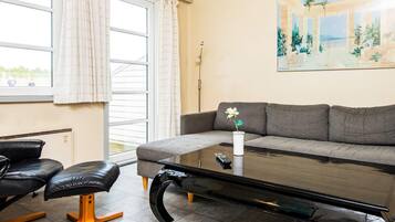 A living room with a grey sofa, a black leather chair, a glass coffee table, and a painting on the wall.
