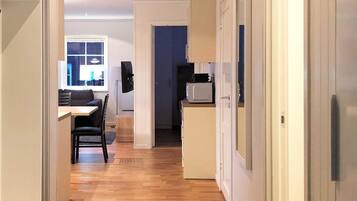 A narrow hallway with a wooden floor leading to a dining area with a table and chairs.