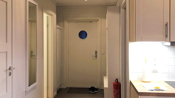 A narrow hallway leading to a door with a circular cut-out, a fire extinguisher mounted on the wall, and a small rug on the floor. - 4 Star Holiday Home in Salen (Salen)