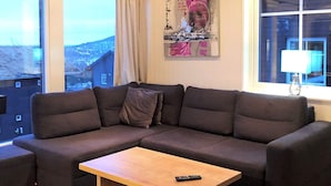A modern living room with a sectional sofa, a wooden coffee table, and a view of a cityscape through large windows. - 4 Star Holiday Home in Salen (Salen)