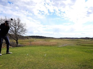 A golf course with a person preparing to hit a golf ball, trees, and a clear sky. - 4 Star Holiday Home in Salen (Salen)