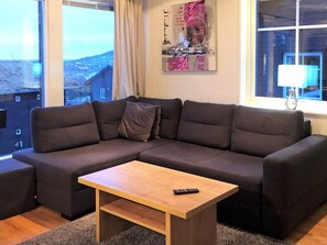 A modern living room with a sectional sofa, a wooden coffee table, and a view of a cityscape through large windows. - 4 Star Holiday Home in Salen (Salen)