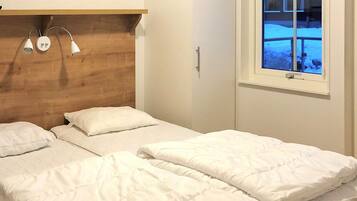 A bedroom with a wooden headboard, two beds with white bedding, a bedside table, and a window with a view of a snowy landscape.