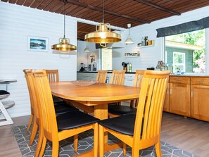 A dining area with a wooden table and chairs, a kitchen in the background, and pendant lighting.