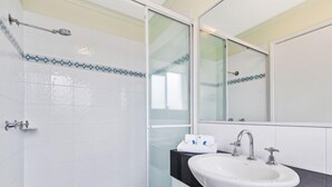 Un bany amb un lavabo blanc, un mirall i una zona de dutxa.