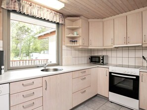 A kitchen with light wood cabinets, a microwave, an oven, a sink, and a window with a view of the outside. - 8 Person Holiday Home in Laeso (Læsø)