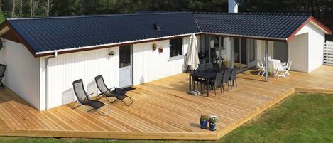 A covered outdoor deck with a table and chairs, a barbecue grill, and a small shed.