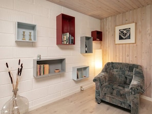 A living room with a patterned armchair, multiple bookshelves, and a framed picture on the wall. - 8 Person Holiday Home in Laeso (Læsø)
