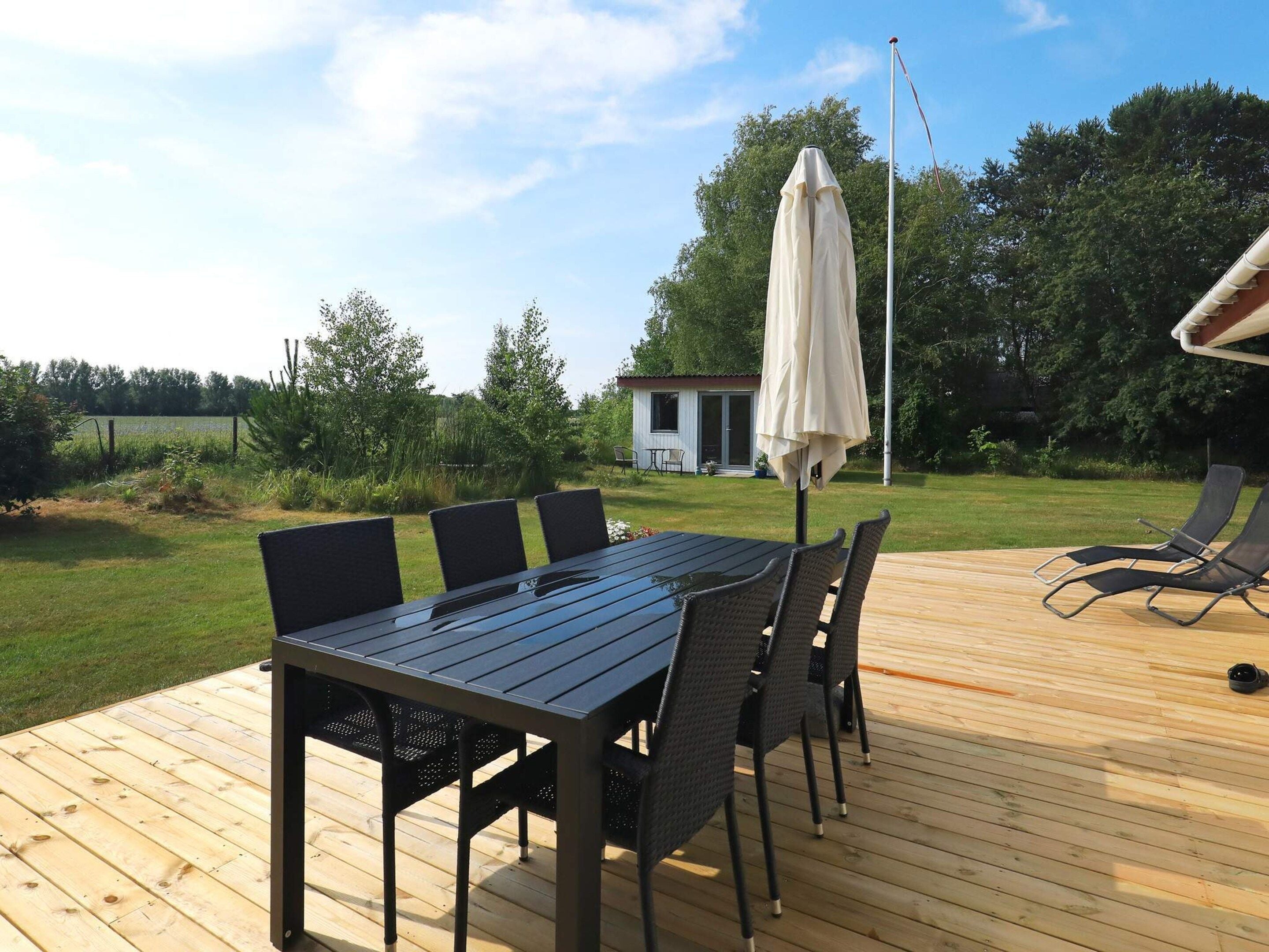 A wooden deck with a table and chairs, an umbrella, and a view of a house and trees in the background.