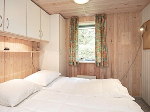 A bedroom with a bed, wooden walls, a window with curtains, and a bedside lamp. - 8 Person Holiday Home in Laeso (Læsø)