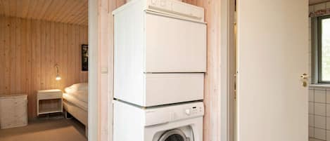 Une petite buanderie équipée d’un lave-linge et d’un sèche-linge superposés, d’une petite table de chevet et d’une fenêtre donnant sur un beau paysage.