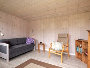 Une pièce comprenant un canapé, un fauteuil, une petite table, une bibliothèque et un plafond en bois.