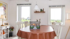 Een eetgedeelte met een ronde tafel, witte stoelen, een rode tafelkleed, een hanglamp en een model van een huis op de tafel.