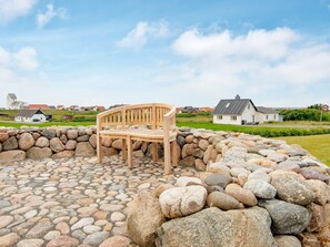A wooden bench in a stone-paved area with a stone wall, surrounded by houses and a clear sky. - 5 Person Holiday Home in Lemvig-by Traum (Lemvig)