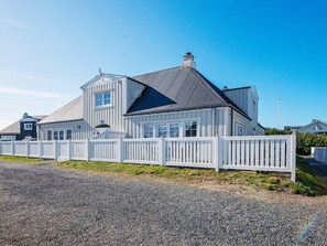A large, two-story house with a white picket fence, a grey roof, and a clear blue sky.