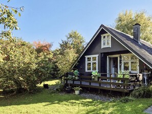 A dark-colored house with a porch, a chimney, and a garden with various plants and a bench. - 5 Person Holiday Home in Odder (Odder)