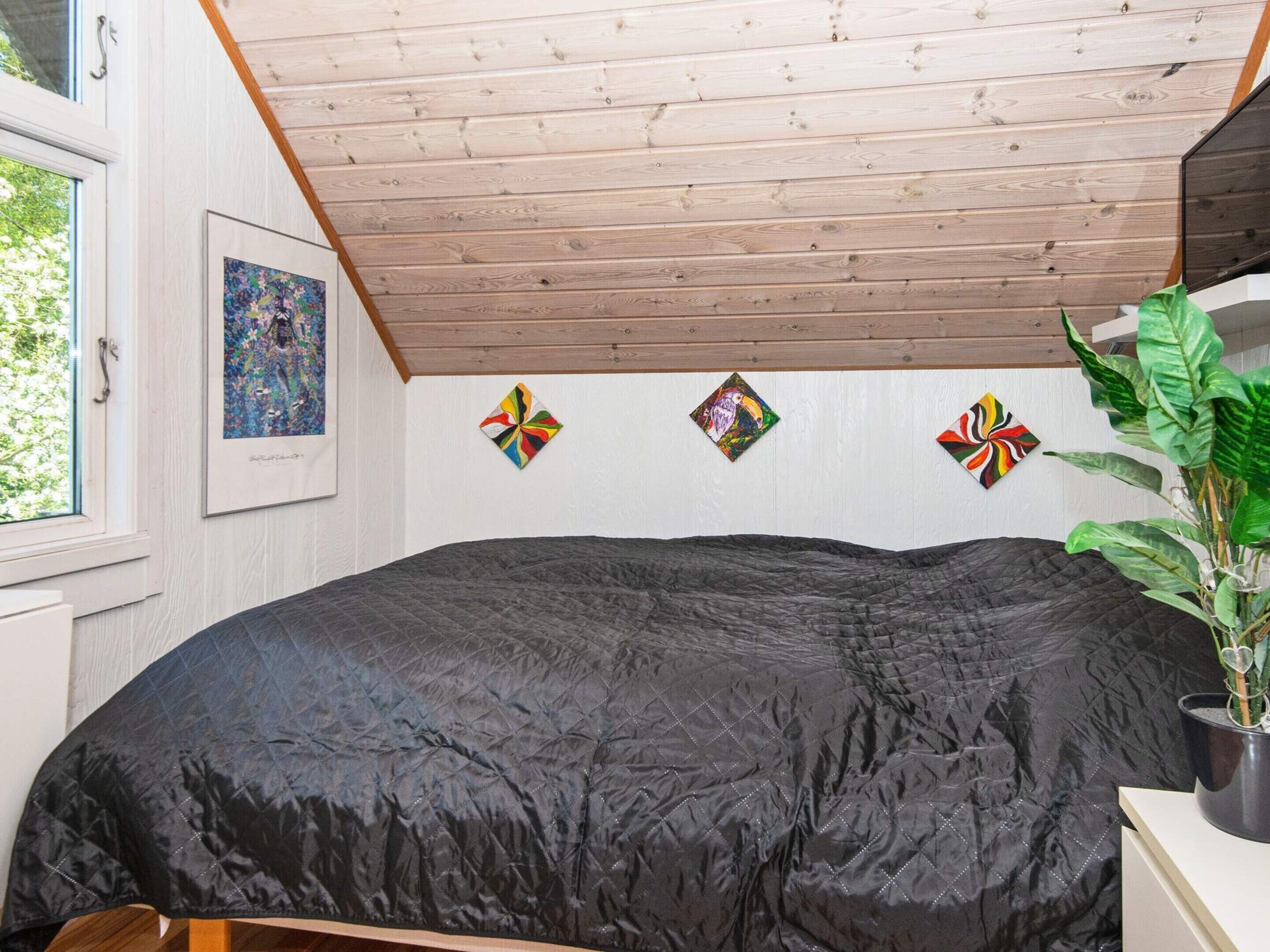 A bedroom with a sloped ceiling, a black quilted bed, and three colorful wall art pieces.