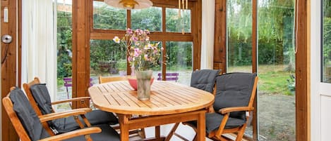 A wooden dining table with four chairs, a vase with flowers, and a view of greenery outside.
