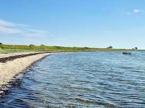 Uma praia com águas cristalinas, um barco e uma linha de costa ao longe.