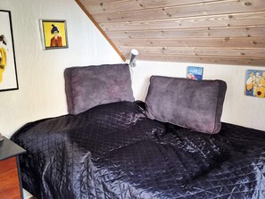A bed with a quilted black cover, wooden ceiling beams, and artwork on the walls. - 5 Person Holiday Home in Odder (Odder)