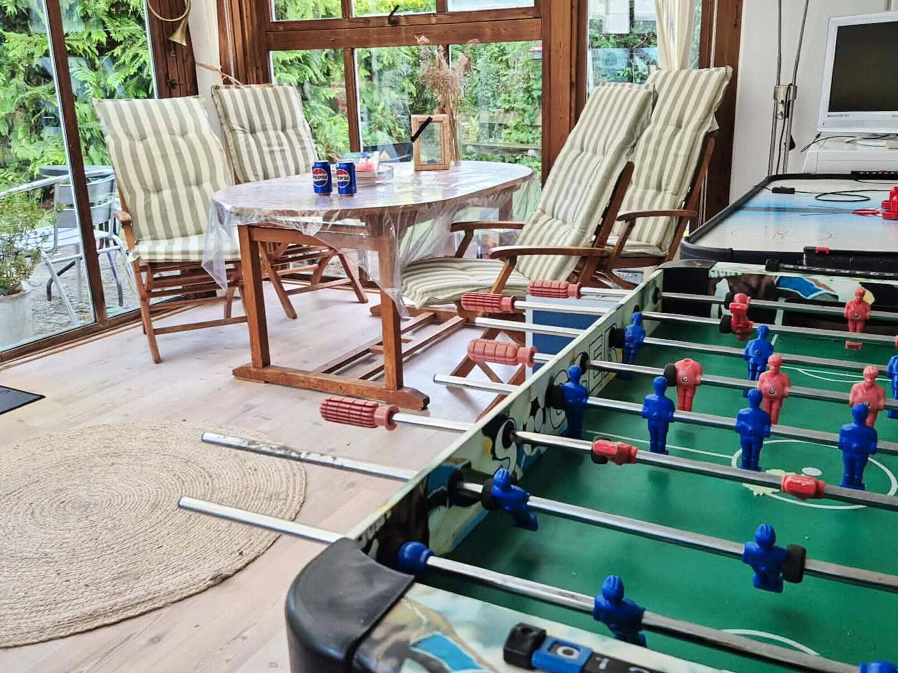 A room with a foosball table, striped chairs, a table with cans, and a TV.